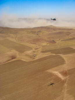 A helicopter and it's shadow, on the perched earth, below with a dust storm in the background.