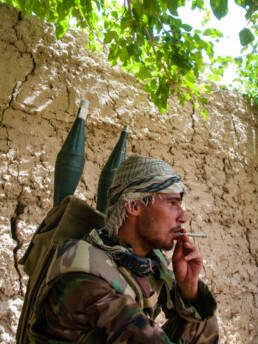 Afghan National Army soldier, with rocket heads attached to his back, having a cigarette break while on patrol in the Green Zone in Helmand, Afghanistan.