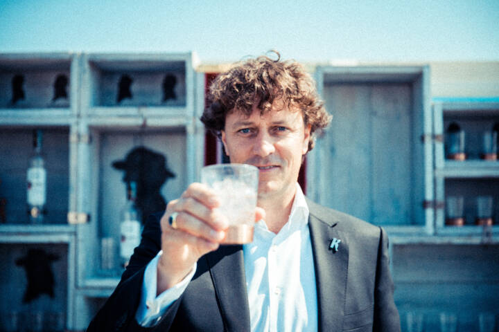 Lifestyle portrait of 1th Generation & Master Distiller Ketel One Bob Nolet in suit at an outdoor bar holding up a glass of vodka to the camera by portrait photographer Andy Barnham