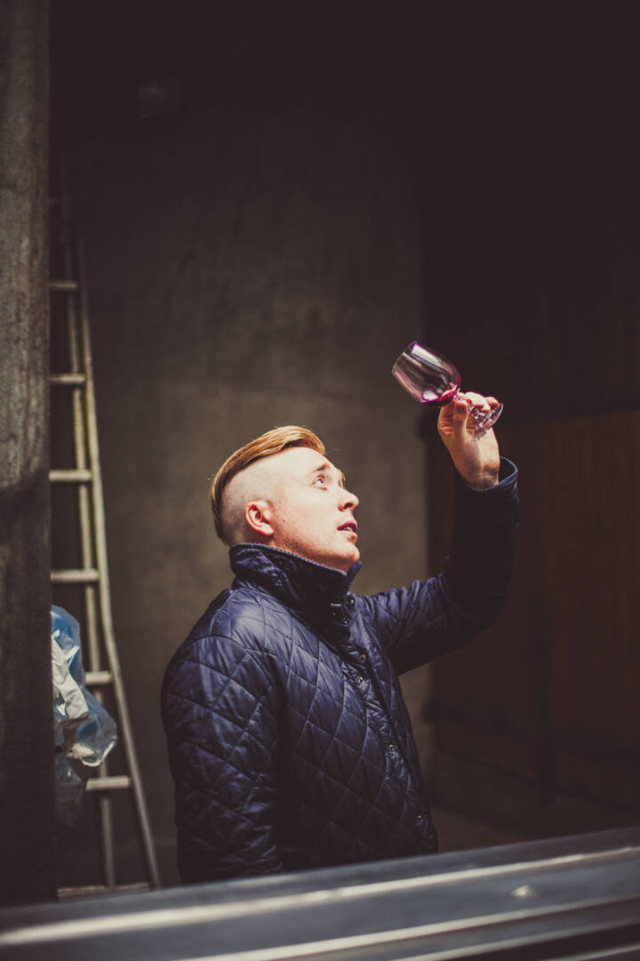 Lifestyle portrait of man in blue coat holding a glass of wine to the light by portrait photographer Andy Barnham