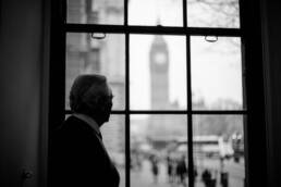 Black and white portrait of Michael Heseltine looking out of his window at the Houses of Parliament