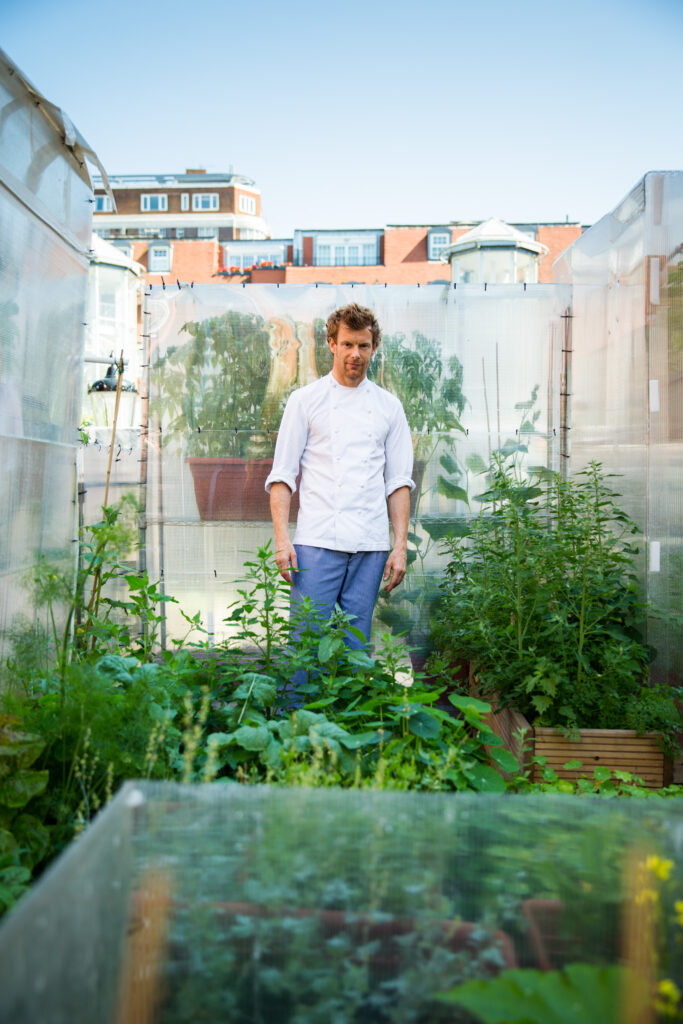 Lifestyle portrait of a English Michelin-starred chef Tom Aikens standing on a rooftop garden with apartment blocks in background by portrait photographer Andy Barnham