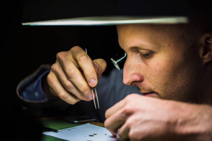 Lifestyle portrait of Vacheron Constantin Maitre Horlogers with eye loupe using tweezers to fix a watch by portrait photographer Andy Barnham