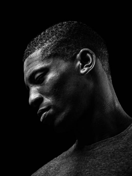 Headshot of an black man with short cropped hair in grey t-shirt in front of a black background by portrait photographer Andy Barnham