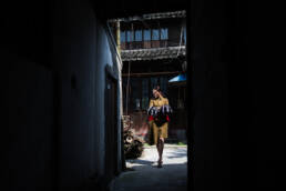 Oriental woman in brown dress walking down an alley away from a wooden shophouse.