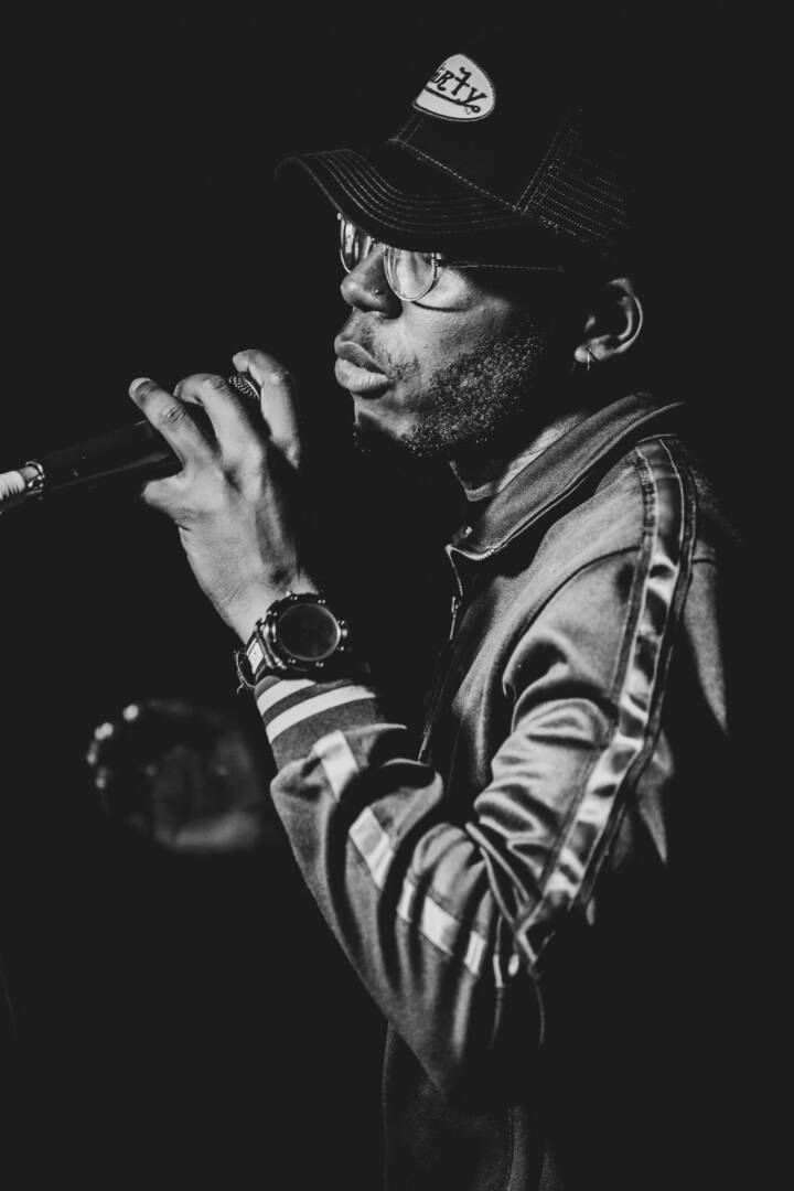 Lifestyle portrait of British rapper Che Lingo with glasses and cap in a track suit top rapping into a microphone by portrait photographer Andy Barnham