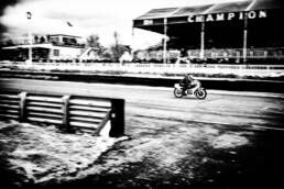 Lone motorbike racing past the control tower and the grandstand, with the word champion, in the background