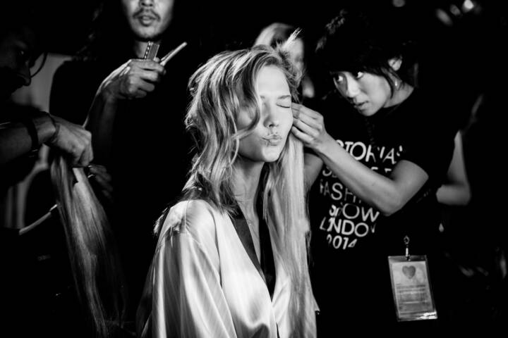 Lifestyle portrait of supermodel Karlie Kloss in dressing gown getting hair and make up blowing a kiss to the camera backstage at Victoria's Secrets fashion show by portrait photographer Andy Barnham