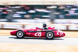 Red Maserati 250F on the track with the grandstand in the background