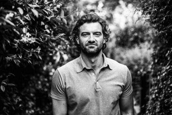 Lifestyle portrait of Scottish actor Stuart Martin in grey tee walking down a garden path surrounded by foliage by portrait photographer Andy Barnham