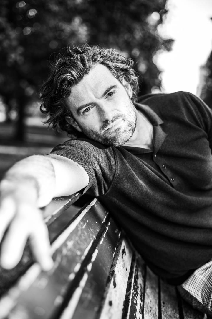 Lifestyle portrait of Scottish actor Stuart Martin in black tee sitting on a park bench by portrait photographer Andy Barnham