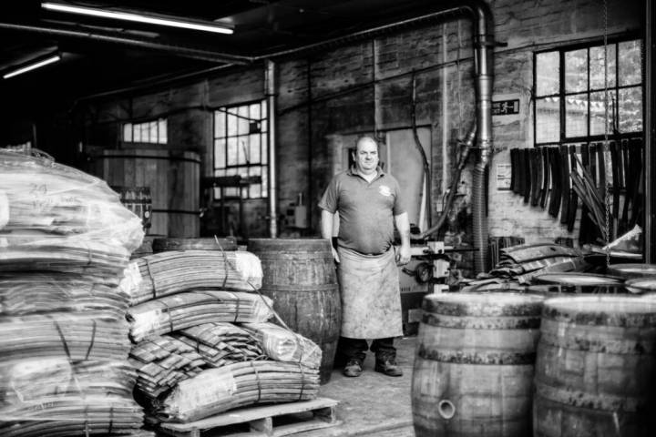 Lifestyle portrait of Master Cooper Alastair Simms wearing an apron surrounded by casks and staves by portrait photographer Andy Barnham