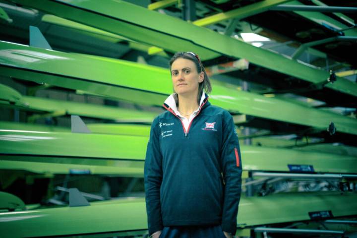 Lifestyle portrait of double Olympic champion Heather Stanning in tracksuit with hands in pockets standing in shed of Olympic rowing boats