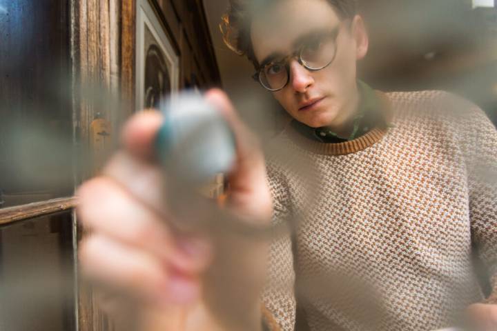 Lifestyle portrait of British interior designer Luke Edward Hall in glasses and white and beige jumper writing on glass by portrait photographer Andy Barnham