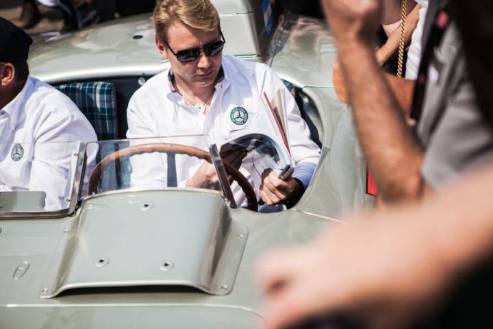 Lifestyle portrait of Formula One World Champion, Mika Häkkinen, wearing sun glasses at the wheel of a classic Mercedes car flicking through a magazine surrounded by a crowd by portrait photographer Andy Barnham