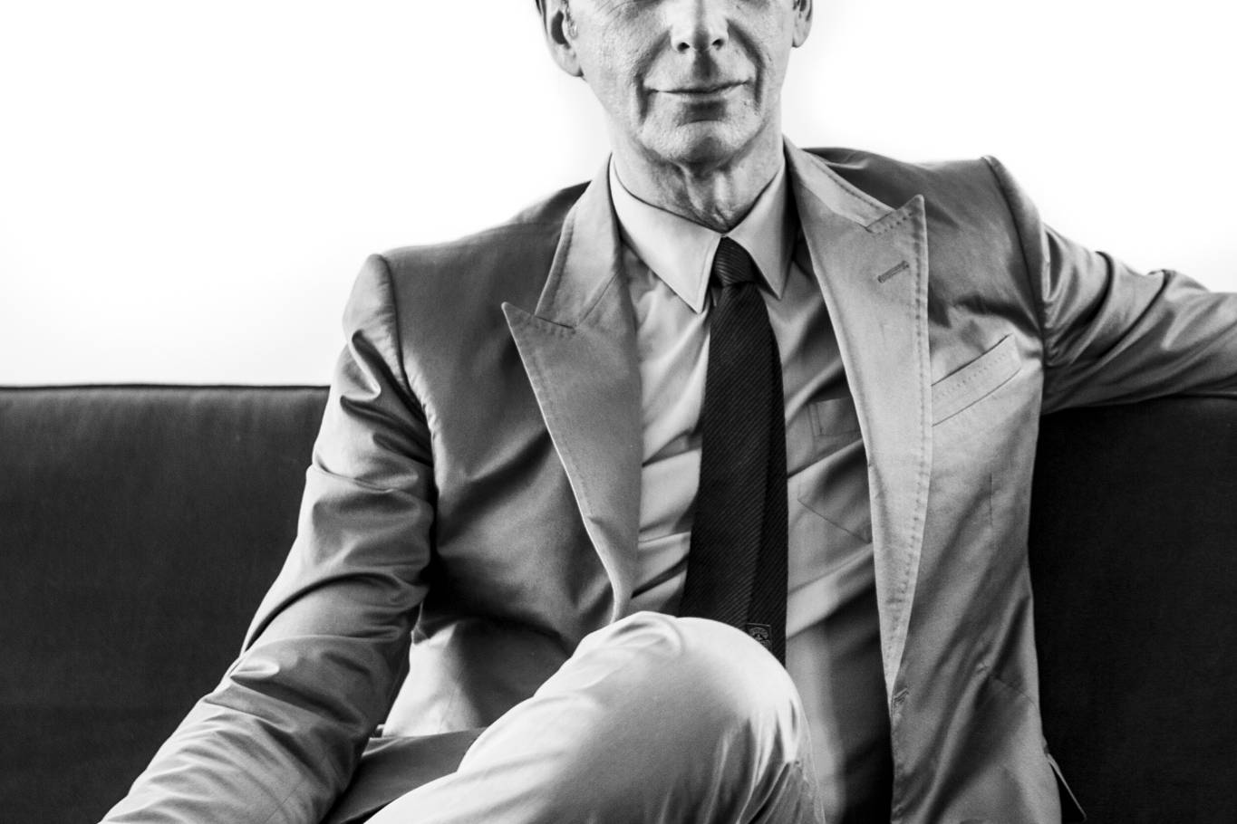 Black and white portrait of former CEO Gucci Patrizio di Marco in a suit sitting on a sofa looking at the camera by portrait photographer Andy Barnham