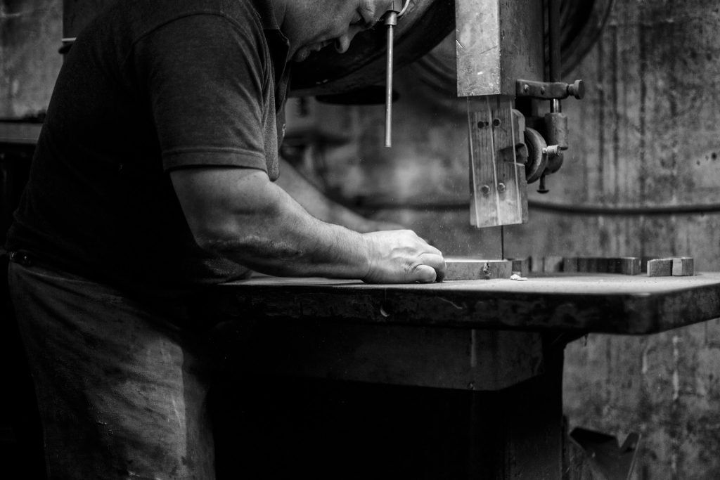 Black and white lifestyle photograph of Master Cooper Alastair Simms cutting wood using a saw by portrait photographer Andy Barnham