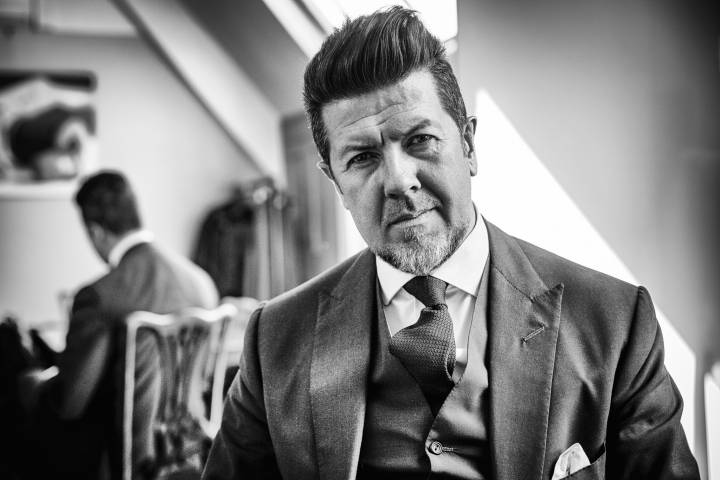 Lifestyle portrait of Savile Row tailor David Ward with beard in three piece suit with reflection of himself in mirror behind by portrait photographer Andy Barnham