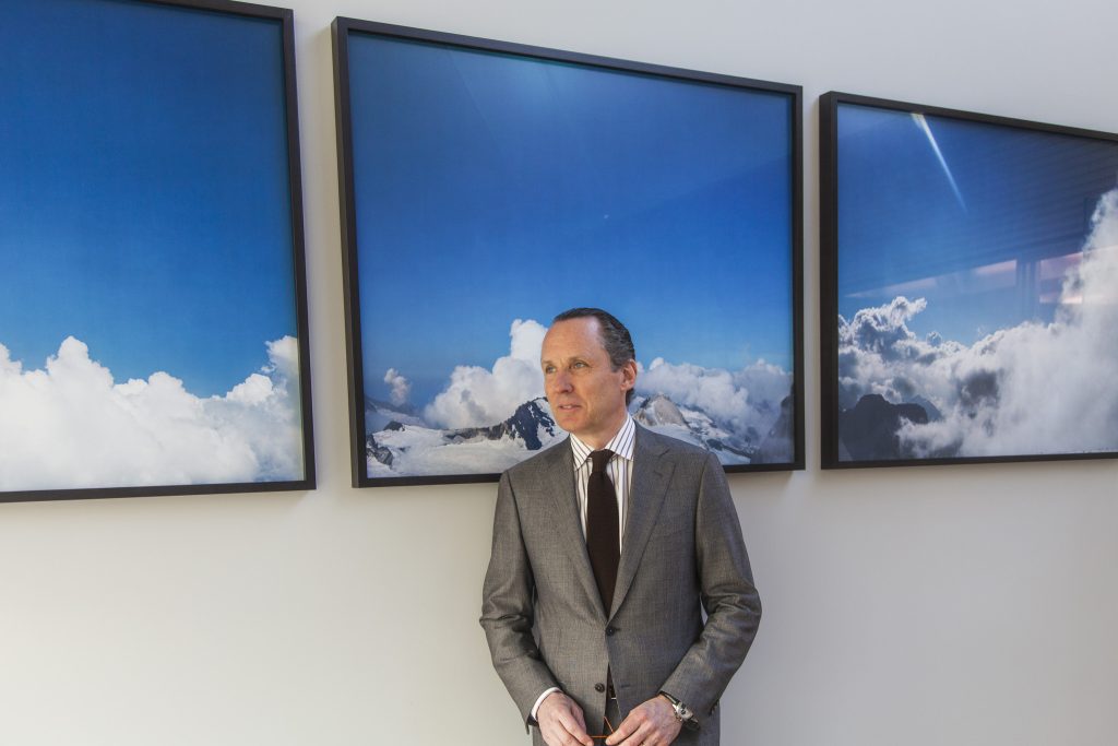 Lifestyle portrait Ermenegildo “Gildo” Zegna, Chairman and CEO of Ermenegildo Zegna Group in suit and tie standing in front of three large framed art works of clouds, skies and mountains by portrait photographer Andy Barnham