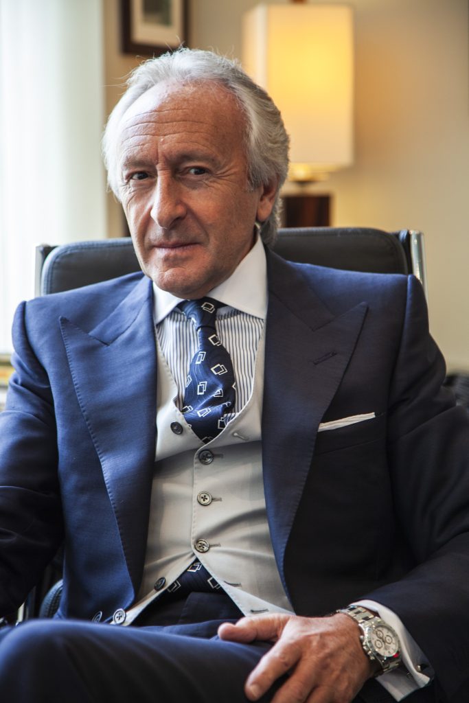 Lifestyle portrait of former chair of the British Fashion Council Harold Tillman in three piece suit wearing a silver Rolex Daytona watch sitting in a high back chair by portrait photographer Andy Barnham