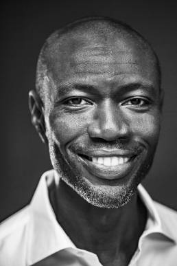 Headshot of an black man in a white shirt in front of a grey background by portrait photographer Andy Barnham