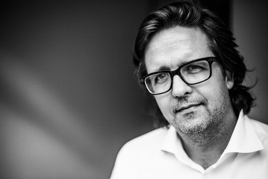 Close up lifestyle portrait of product designer Christoph Behling wearing black rim glasses and a white shirt in a doorway by portrait photographer Andy Barnham