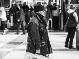 Black and white photo of a man, standing in a train station, holding a sign saying welcome to pig city