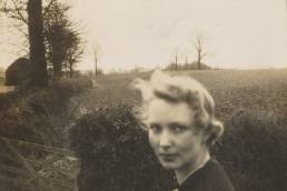 Black and white photo of woman with blonde hair next to a gate and field behind