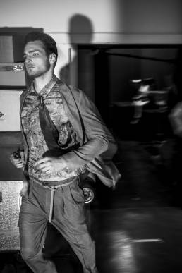 Backstage at Emporio Armani, designed by Giorgio Armani, a male model runs into the backstage area in order to change looks during a fashion show by Andy Barnham