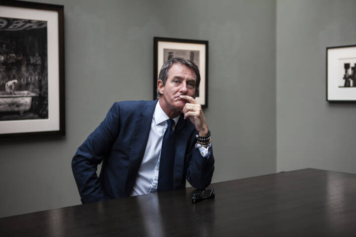 Lifestyle portrait of Director of Hamiltons Gallery Tim Jeffries with his hand on his chin sitting a a table with fine art photography prints in background by portrait photographer Andy Barnham