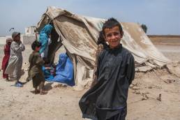 Boy standing in front of a dust covered tent full of women and children