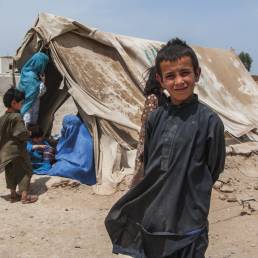 Boy standing in front of a dust covered tent full of women and children
