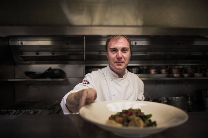 Lifestyle portrait of chef in kitchen serving a plate of pasta by portrait photographer Andy Barnham