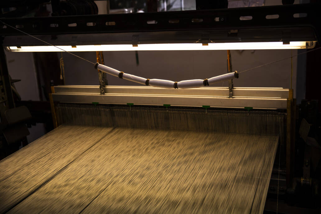 Renaissance era cloth loom with spools of white thread under a fluorescent light