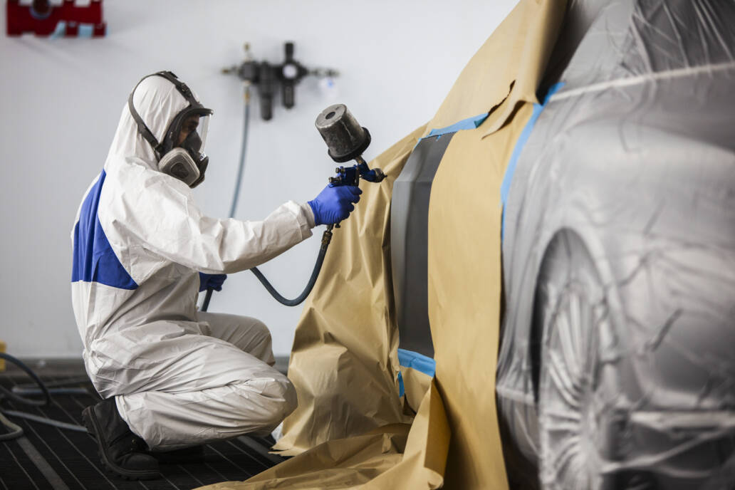 Man in white protective clothing spray painting a car