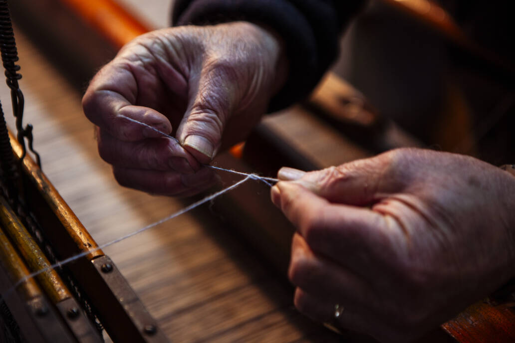 Hands tying a knot unthread over a manual wooden loom