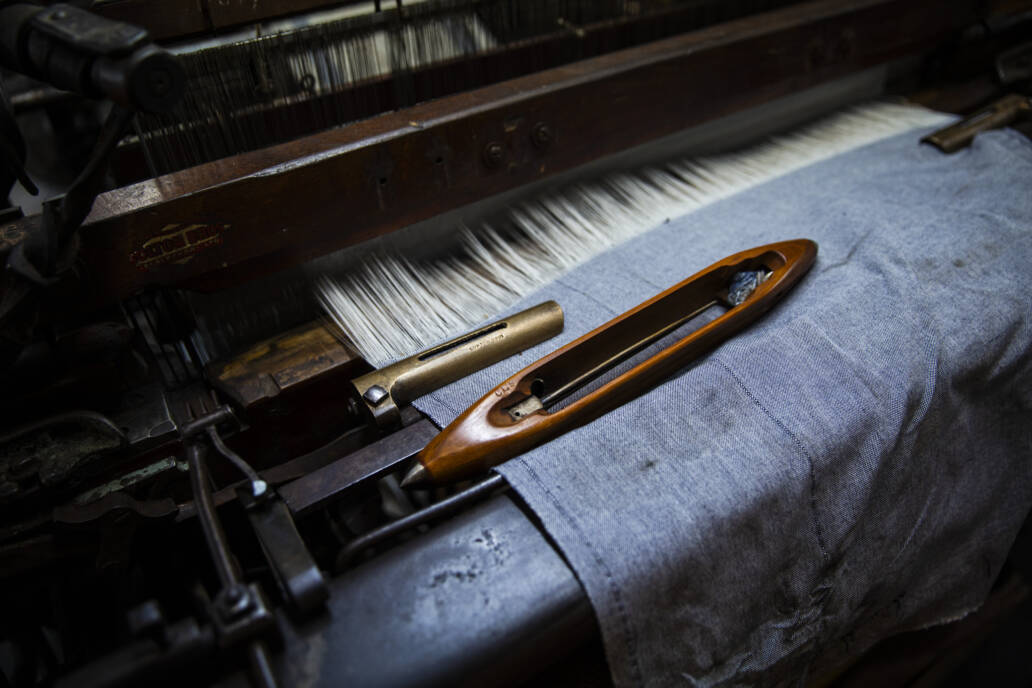 Shuttle sitting on a half woven piece of cloth on a wooden loom