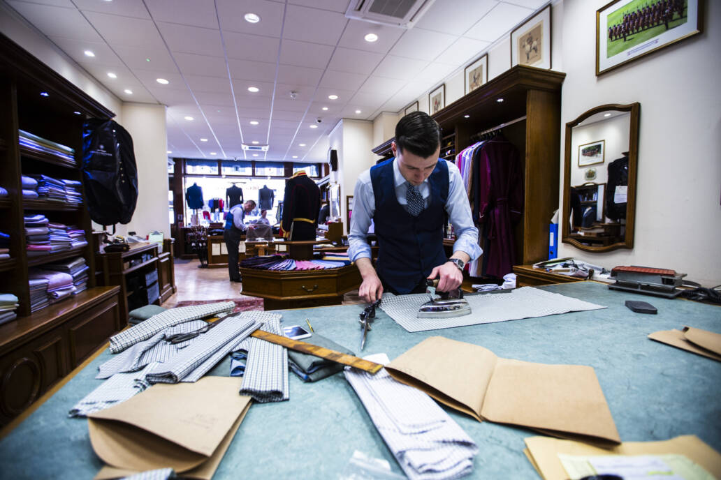 Bespoke shirt maker working at a bench with shop in background
