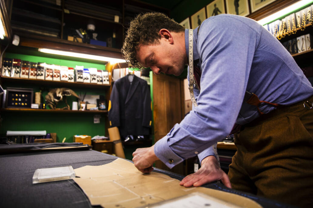 Bespoke tailor at work bench chalking up a pattern on a piece of cloth