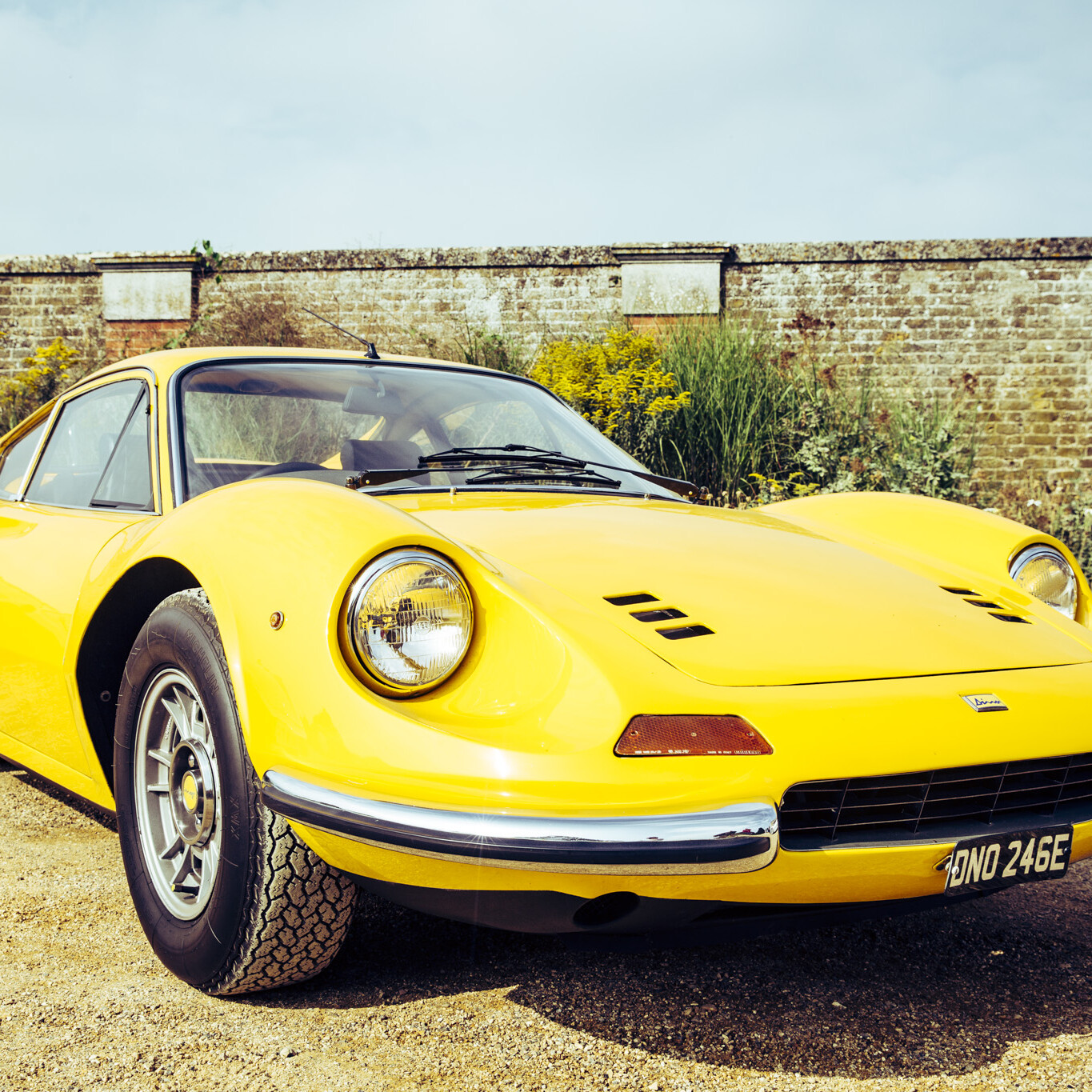 Yellow classic sports car in front of high brick wall