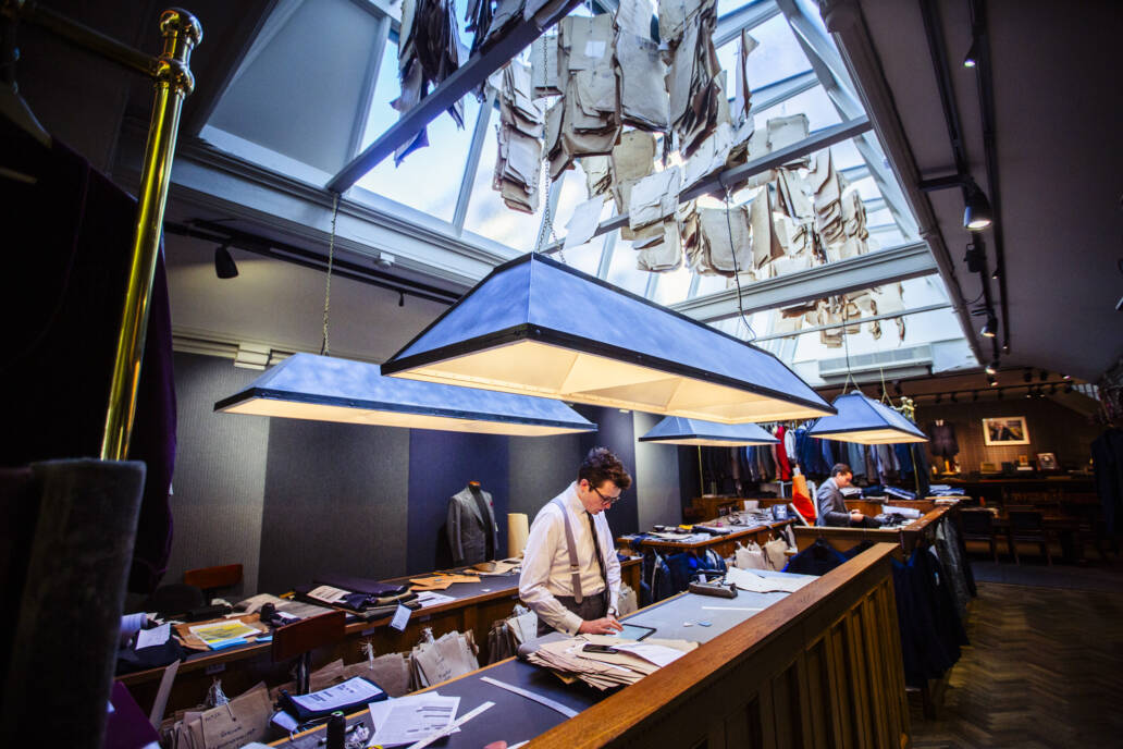 Bespoke tailors working under skylit with suit patterns hanging in the rafters