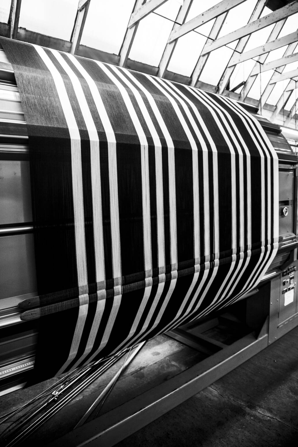 Striped black and white fabric being woven on a loom under a skylight