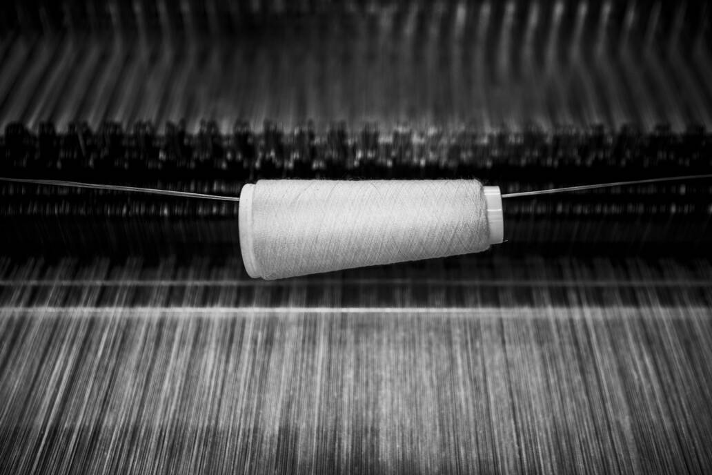 Yarn of white thread over a loom with tenterhooks in the background.