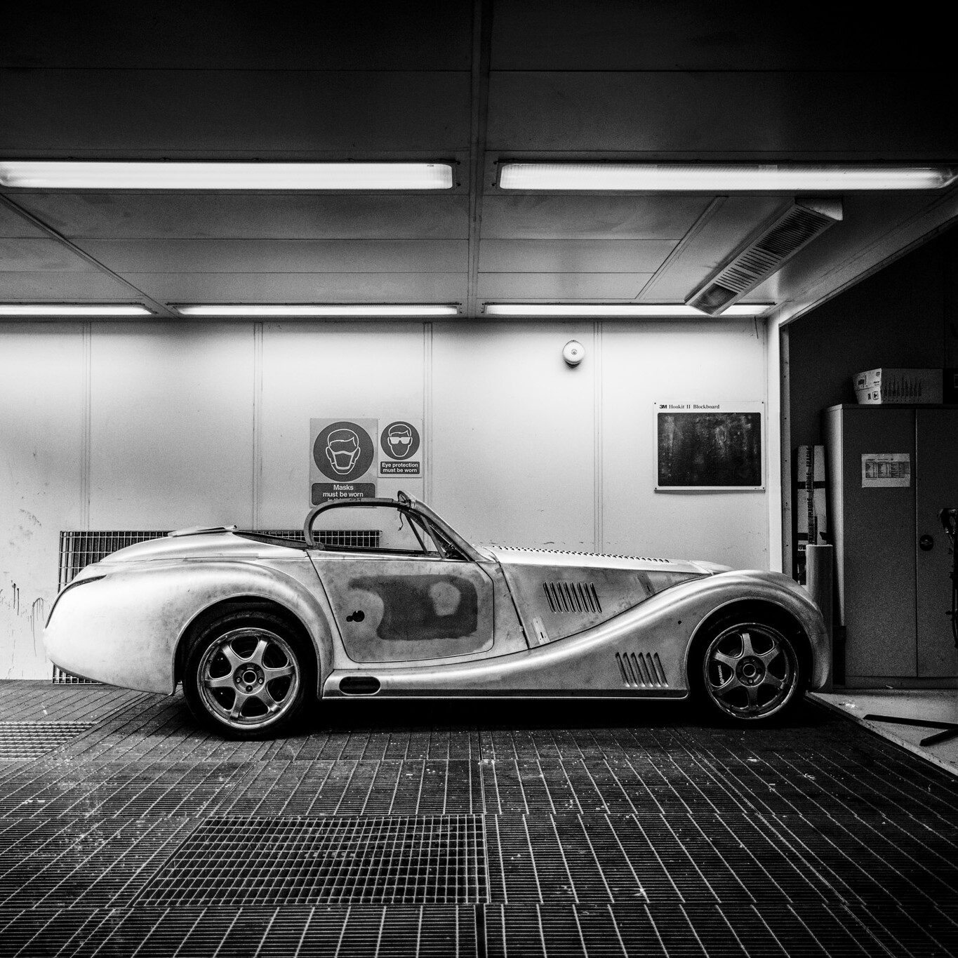 Unpainted sports car under construction on metal grills in a paint shop