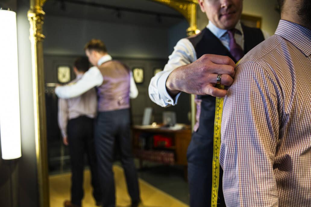 Tailor measuring a man's shoulders in front of a mirror