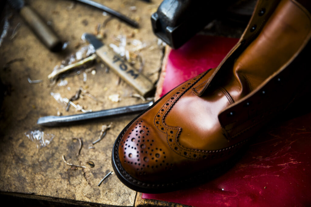 Tan brogue boot without laces on worktop bench with tools