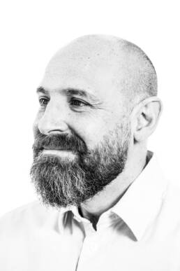 Headshot of bald man with a beard against a white backdrop looking to his right